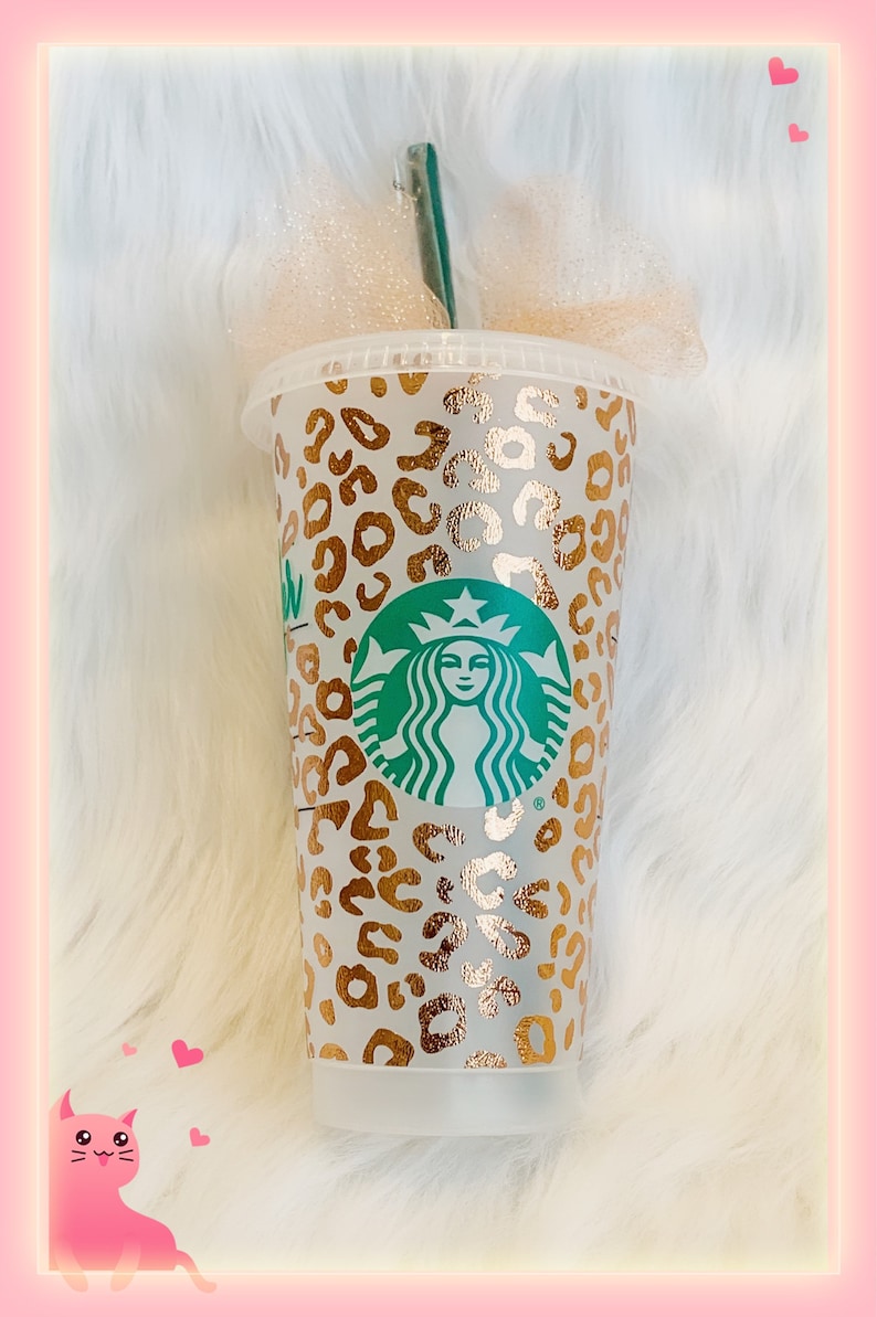 May include: A clear plastic reusable cup with a gold and white leopard print design. The cup has the Starbucks logo in green and white on the front.