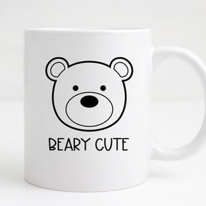 May include: White ceramic mug featuring a black outline illustration of a bear's face. The text "BEARY CUTE" is printed below the bear design. The mug has a curved handle.