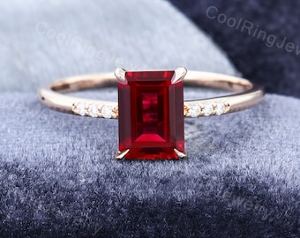 Op de afbeelding: Een verlovingsring van roségoud met een rode smaragd geslepen edelsteen en een band met kleine diamanten.