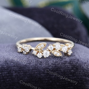 May include: A delicate gold ring with a floral design featuring small, sparkling diamonds. The ring is set on a soft, gray fabric background.