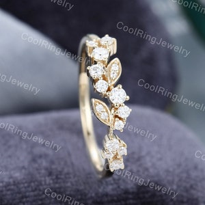 Op de afbeelding: Een delicate gouden ring met een bloemmotief met kleine, glinsterende diamanten. De ring ligt op een grijze achtergrond.