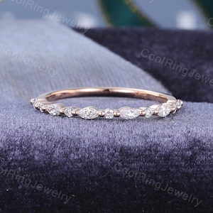 May include: A rose gold band ring featuring an alternating pattern of marquise-cut and round-cut clear stones set along the top half of the band. The metal has a smooth, polished finish, and the stones are arranged in a symmetrical, repeating sequence.