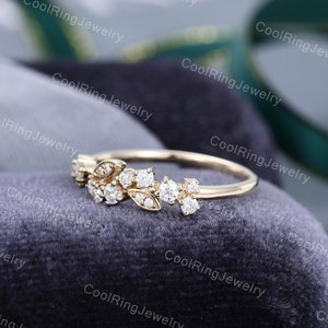 Op de afbeelding: Een delicate gouden ring met een bloemmotief met kleine, glinsterende diamanten. De ring ligt op een grijze fluwelen achtergrond.