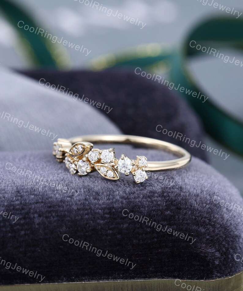 Op de afbeelding: Een delicate gouden ring met een bloemmotief met kleine, glinsterende diamanten. De ring ligt op een grijze fluwelen achtergrond.