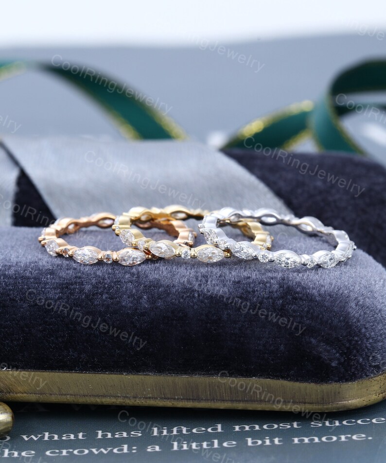 May include: Three eternity bands with marquise-shaped diamonds set in a pave setting. The bands are in white gold, yellow gold, and rose gold.