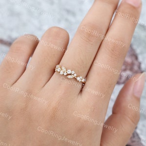 Op de afbeelding: Een delicate gouden ring met een bloemmotief met kleine, heldere edelstenen. De ring zit aan een vinger.