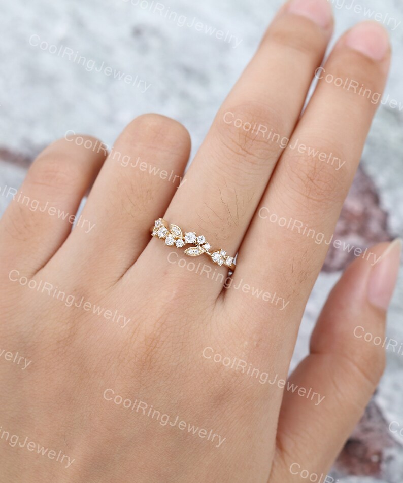 Op de afbeelding: Een delicate gouden ring met een bloemmotief met kleine, heldere edelstenen. De ring zit aan een vinger.