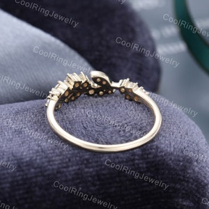 Op de afbeelding: Een delicate gouden ring met een bladontwerp en kleine glinsterende stenen. De ring ligt op een grijze fluwelen achtergrond.