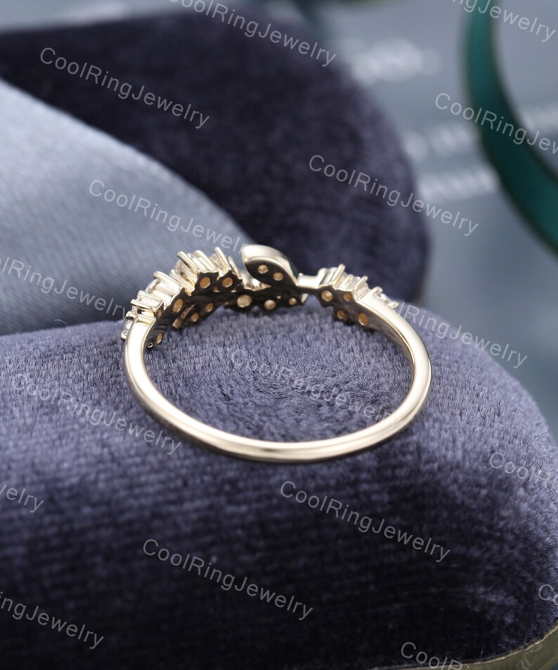 Op de afbeelding: Een delicate gouden ring met een bladontwerp en kleine glinsterende stenen. De ring ligt op een grijze fluwelen achtergrond.