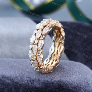 May include: A gold wedding band with a double row of marquise-shaped diamonds. The diamonds are set in a pave setting and are surrounded by smaller round diamonds.