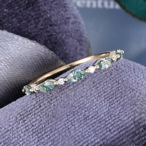 May include: A gold band ring featuring a series of alternating marquise-cut moss agate stones and small round clear stones. The moss agate stones display green inclusions within a translucent body, set along the thin, polished gold metal band.