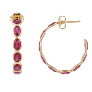 May include: A pair of gold hoop earrings featuring a series of oval-shaped, deep pink gemstones set in a continuous row along the front of each hoop. The earrings include a standard post and clutch backing mechanism for secure attachment to the ear.