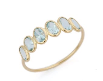 May include: A gold ring featuring a row of six oval-cut light blue gemstones set in a delicate band. The stones are arranged in a graduated size pattern, with the central stones being slightly larger than those at the ends of the setting.