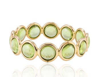 May include: A gold ring with a band of round green gemstones. The ring is set with a row of 10 stones.