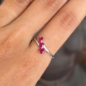 May include: A silver ring featuring three oval-cut, vibrant red gemstones. The gemstones are set in a cluster design, creating a delicate and eye-catching piece of jewelry. The ring's band has a subtle, textured appearance.
