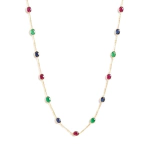 May include: A delicate gold chain necklace featuring evenly spaced, oval-cut gemstones in alternating colors of deep red, vibrant green, and dark blue. The stones are set in simple metal bezels along the length of the thin, polished gold link chain.