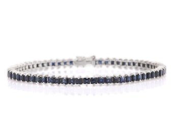 May include: A silver tennis bracelet with a row of square-shaped blue sapphires.