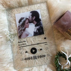 Könnte beinhalten: Transparente Glasplakette mit einem Foto eines sich küssenden Paares. Die Plakette hat ein Musikplayer-Oberflächendesign mit dem Song "Marry You" von Bruno Mars und einem QR-Code.