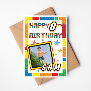 May include: A birthday card with a photo of a child jumping, surrounded by a colorful border of toy building blocks. The card reads "HAPPY 8TH BIRTHDAY SAM" in a playful font, with star accents. The card is on a brown envelope.