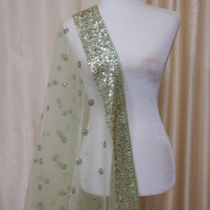 May include: A light green sheer shawl with a gold and green embroidered border. The shawl is decorated with small floral patterns.