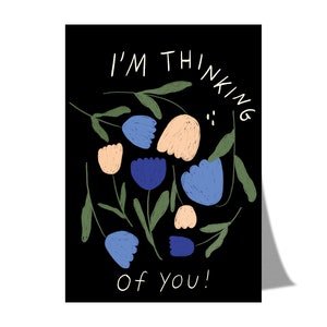 Könnte beinhalten: Eine schwarze Karte mit weißem Text, der "Ich denke an dich!" lautet, umgeben von grünen Blättern und blauen und pfirsichfarbenen Blumen.
