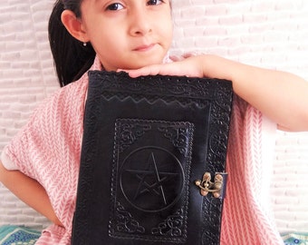 May include: A young person holding a black leather journal with a pentagram design and a brass clasp.