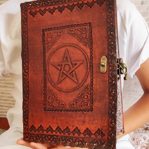 May include: A brown leather journal with a pentagram design and a metal clasp. The journal has intricate embossed details around the edges.