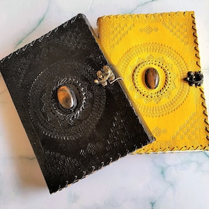 May include: Two leather-bound journals with decorative designs and gemstone accents. One journal is black with a brown gemstone, and the other is yellow with a brown gemstone.