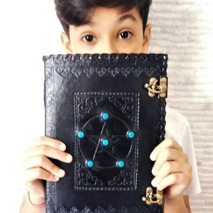 May include: A black leather journal with a pentagram design and turquoise gemstones. The journal has two brass clasps and is embossed with intricate patterns.