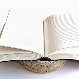 May include: A black leather-bound journal with lined pages, open to reveal the blank pages. The journal is resting on a woven straw mat.