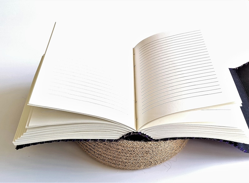 May include: A black leather-bound journal with lined pages, open to reveal the blank pages. The journal is resting on a woven straw mat.