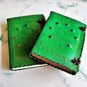 May include: Two green leather journals with tree of life designs and gemstone accents. The journals have decorative stitching and metal clasps.