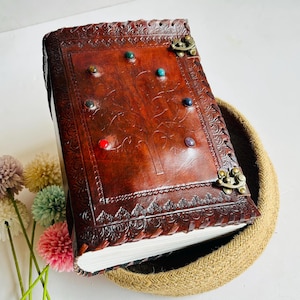 Peut inclure: Un journal en cuir marron avec un motif d'arbre et des pierres précieuses colorées incrustées dans la couverture. Le journal a une fermeture à fermoir et est décoré de détails en relief complexes.