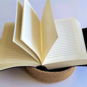 May include: A purple leather-bound journal with lined pages, open and resting on a woven jute base.