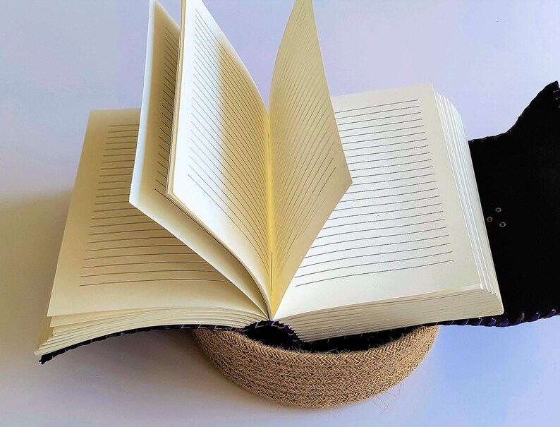 May include: A purple leather-bound journal with lined pages, open and resting on a woven jute base.