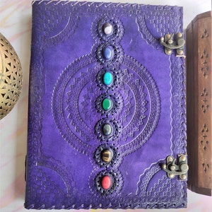 May include: Purple leather journal with intricate embossed designs and seven colorful gemstones set into the cover. The journal has two metal clasps.