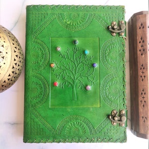 Peut inclure: Journal en cuir vert avec un motif d'arbre et des pierres précieuses colorées. Le journal a deux fermoirs métalliques et des coutures décoratives autour des bords.