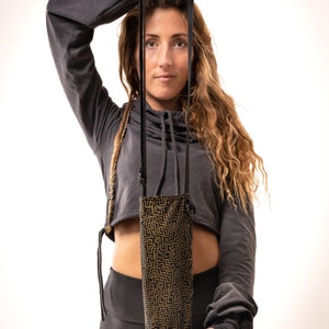 May include: A black and gold patterned water bottle holder with a black strap. The holder is held up by a person. The holder has a geometric design in gold on a black background. The strap is black and appears to be adjustable.