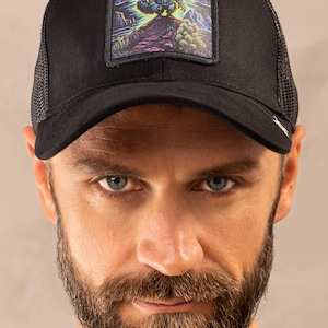 Può includere: Cappellino da camionista nero con retro in rete e toppa quadrata con illustrazione di un procione. Il procione è su una collina con un paesaggio colorato. Il cappellino ha una visiera curva.