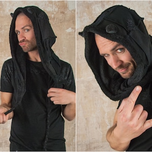 May include: A black hooded garment with a furry lining and ear-like flaps. The hood is pulled up over the head of the person wearing it.