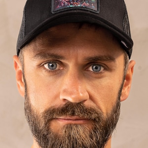 Può includere: Cappellino da camionista nero con retro in rete e una toppa colorata con un design dettagliato di creature fantastiche. Il cappellino ha una visiera curva e una chiusura a scatto regolabile.