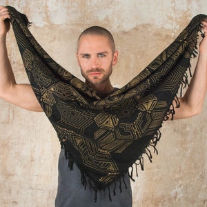 May include: A person wearing a black and gold patterned scarf with fringe. The scarf has a geometric design.