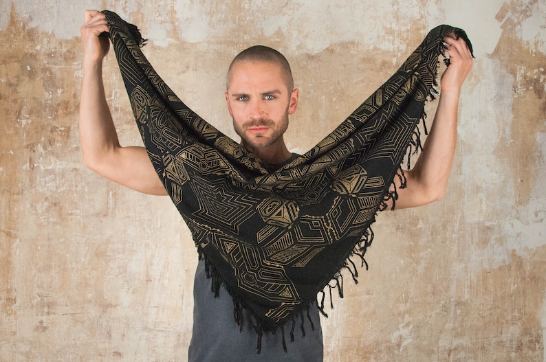 May include: A person wearing a black and gold patterned scarf with fringe. The scarf has a geometric design.