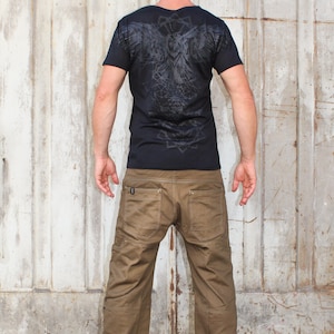 May include: A man wearing a black t-shirt with a geometric owl design on the back and brown cargo pants.