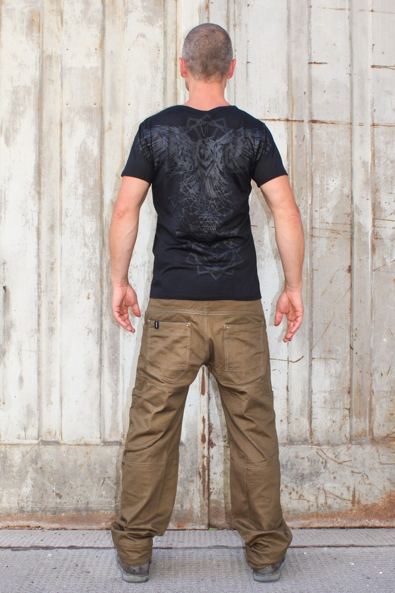 May include: A man wearing a black t-shirt with a geometric owl design on the back and brown cargo pants.