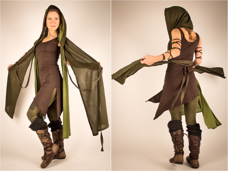 May include: A woman wearing a brown and green hooded tunic with a long green scarf. The tunic has a long, flowing skirt and a fitted bodice. The scarf is tied around the waist and flows behind the woman.