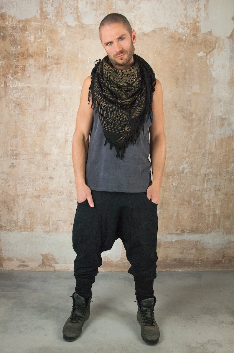May include: A man wearing a black tank top with a black and gold patterned scarf, black pants, and black boots.