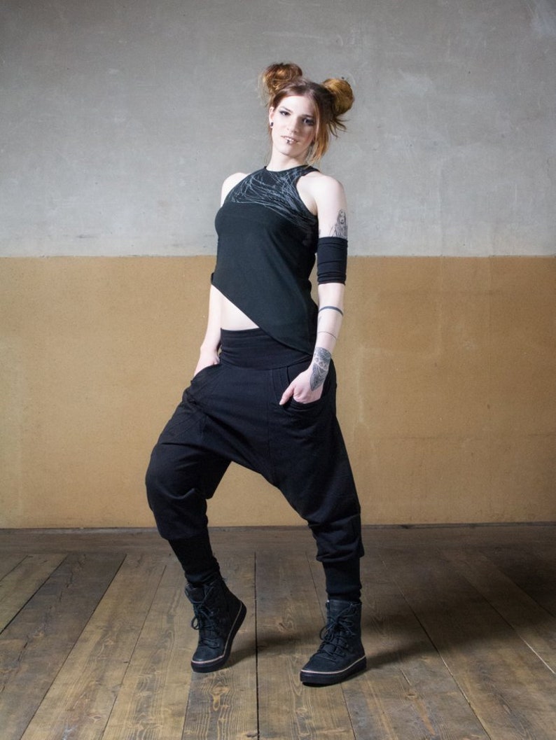 Puede incluir: Una mujer con un top negro asim&eacute;trico con un dise&ntilde;o blanco y pantalones negros. Lleva botas negras y tiene el pelo recogido en dos mo&ntilde;os.
