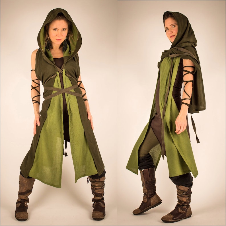 May include: A woman wearing a green hooded cloak with brown leather straps and brown boots. The cloak is tied at the waist and has a long, flowing skirt.