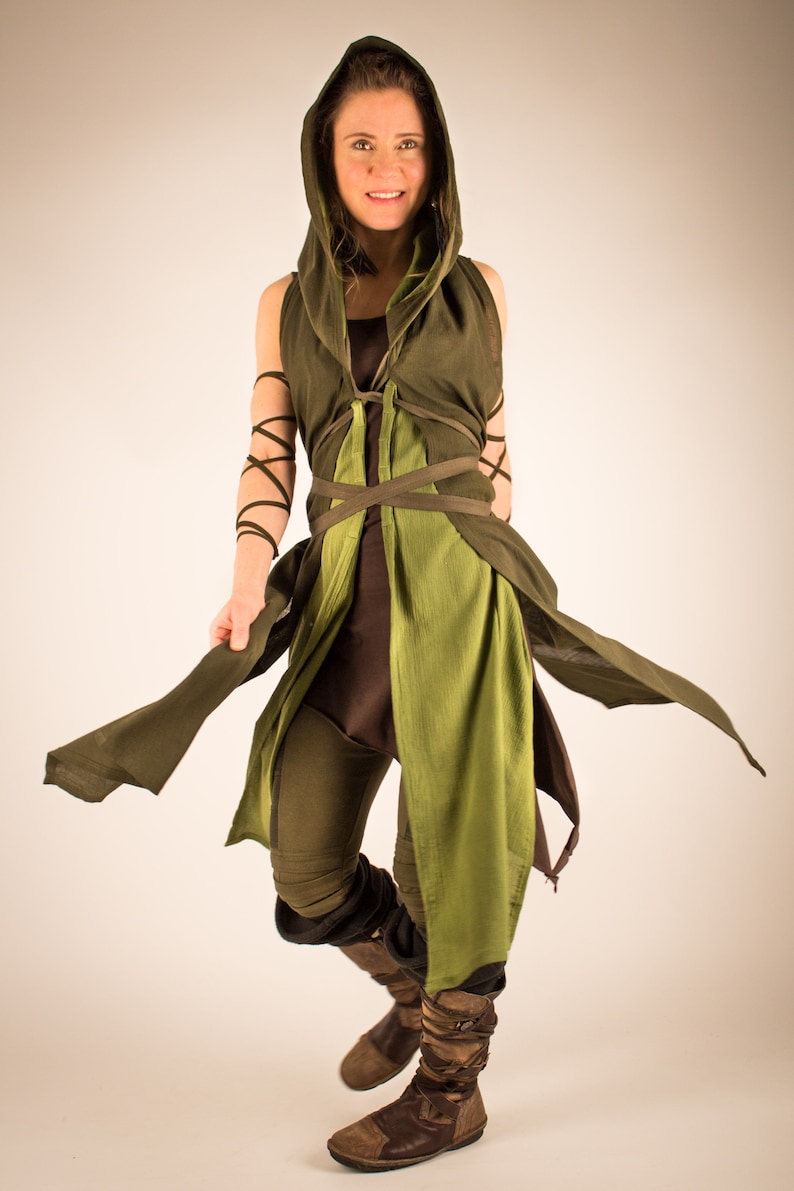 May include: A woman wearing a green hooded tunic with brown pants and brown boots. The tunic has a green and brown color scheme and is tied with a brown belt.